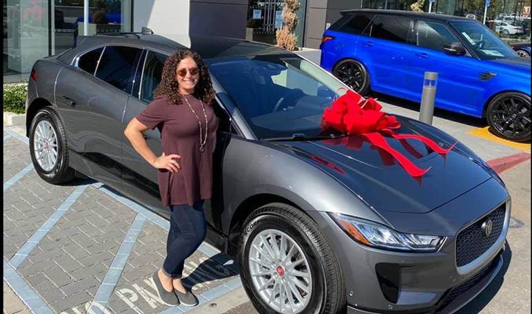 Karen proudly standing next to her new Jaguar i-Pace with large red bow